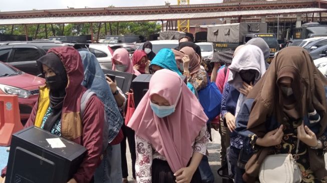 Pekerja pinjol ilegal yang diamankan dari sebuah tempat di Yogyakarta tiba di markas Polda Jawa Barat, Kota Bandung, Jumat (15/10/2021) siang. [Suara.com/Cesar Yudistira]