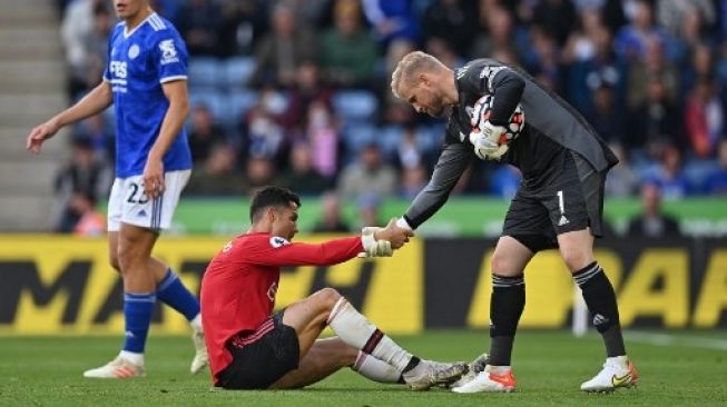 Pemain Manchester United Cristiano Ronaldo dibantu berdiri oleh kiper Leicester City Kasper Schmeichel dalam pertandingan Liga Premier yang digelar di King Power Stadium, Sabtu (16/10/2021). [AFP]