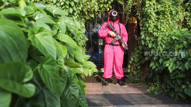 Pramusaji yang menggunakan kostum dari film Squid Game menunggu pengunjung di pintu masuk di Strawberry Cafe, Jakarta Barat, Sabtu (16/10/2021). [Suara.com/Alfian Winanto]