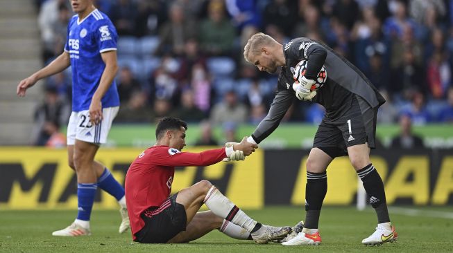 Striker Manchester United Cristiano Ronaldo (tengah) dibantu oleh penjaga gawang Leicester City Kasper Schmeichel (kanan) setelah kehilangan peluang untuk Manchester United selama pertandingan sepak bola Liga Premier Inggris antara Leicester City dan Manchester United di King Power Stadium, Leicester, Inggris pada (16/10/2021). [PAUL ELLIS / AFP]