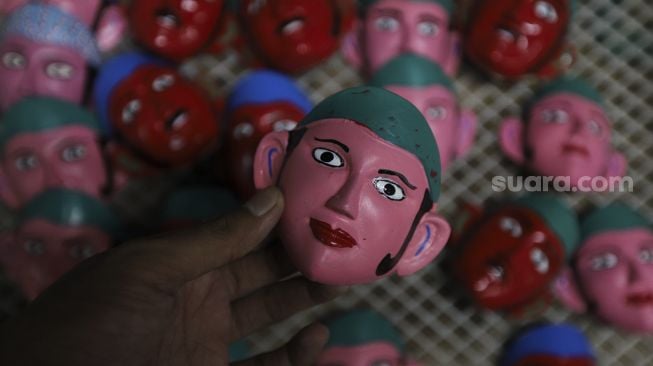 Perajin menunjukkan miniatur topeng ondel-ondel di tokonya di Jalan Gang 3, Pondok Kopi, Kecamatan Duren Sawit, Jakarta, Senin (18/10/2021). [Suara.com/Angga Budhiyanto]