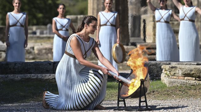 Aktris Yunani Xanthi Georgiou, yang berperan sebagai High Priestess, menyalakan obor selama upacara penyalaan api untuk Olimpiade Musim Dingin Beijing 2022 di situs arkeologi Olympia Kuno, Yunani, pada (18/10/2021). [ARIS MESSINIS / AFP]