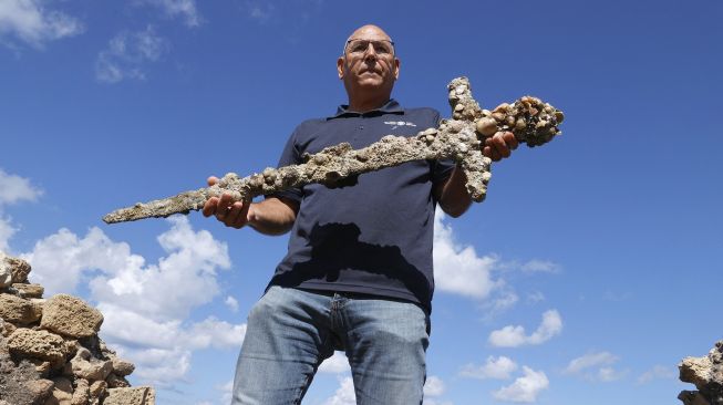 Jacob Sharvit dari Israel Antiquities Authority menunjukkan pedang kuno yang diyakini milik Tentara Salib, di Pelabuhan Israel Kaisarea, pada (19/10/2021).(19/10/2021). [JACK GUEZ / AFP]