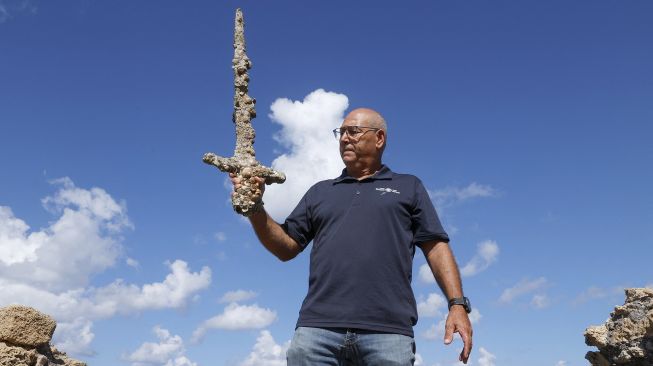 Jacob Sharvit dari Israel Antiquities Authority menunjukkan pedang kuno yang diyakini milik Tentara Salib, di Pelabuhan Israel Kaisarea, pada (19/10/2021).(19/10/2021). [JACK GUEZ / AFP]