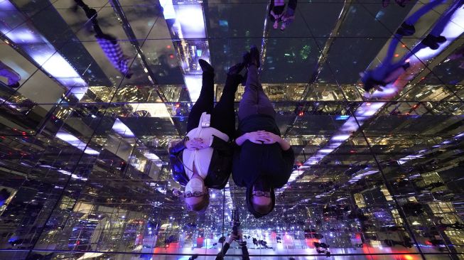 Pengunjung berbaring di permukaan cermin saat anggota media menghadiri press preview untuk mengunjungi 'SUMMIT by Night' menjelang grand opening 'SUMMIT One Vanderbilt' di New York, pada (18/10/2021). [TIMOTHY A. CLARY / AFP]