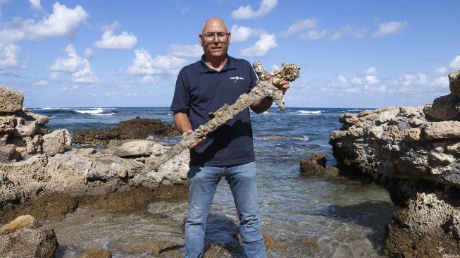 Jacob Sharvit dari Israel Antiquities Authority menunjukkan pedang kuno yang diyakini milik Tentara Salib, di Pelabuhan Israel Kaisarea, pada (19/10/2021).(19/10/2021). [JACK GUEZ / AFP]