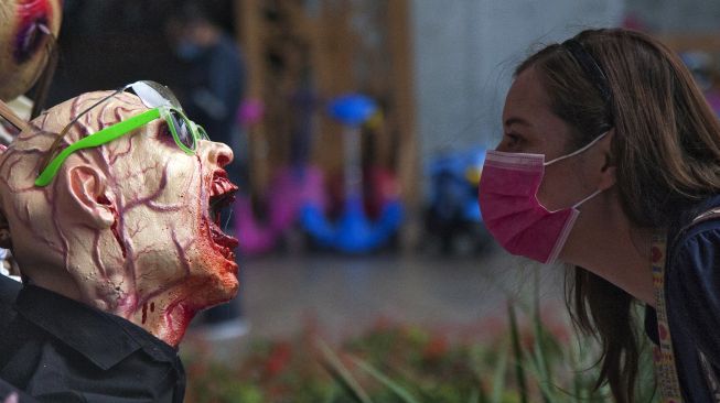 Seorang warga mengamati sosok zombie yang dipajang di pusat perbelanjaan sebagai bagian dari dekorasi Musim Halloween di San Pedro Garza, Nuevo Leon, Meksiko, pada (22/10/2021). [JULIO CESAR AGUILAR / AFP]