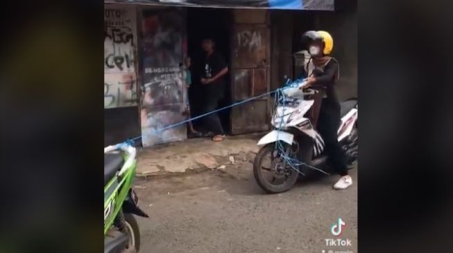 Sebuah video yang memperlihatkan seorang cewek yang sedang menaiki motor ditarik menggunakan tali rafia, viral di media sosial. [Foto: tangkapan layar TikTok]