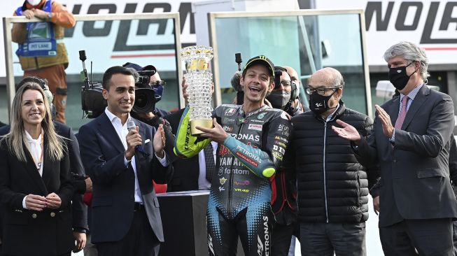 Pembalap Yamaha-SRT Italia Valentino Rossi (tengah) memegang penghargaan seumur hidup karir yang diserahkan kepadanya oleh Menteri Luar Negeri Italia, Luigi Di Maio (kiri) setelah Grand Prix MotoGP Emilia-Romagna di Sirkuit Dunia Misano Marco- Simoncelli, Misano Adriatico, Italia, pada (24/10/2021). [ANDREAS SOLARO / AFP]