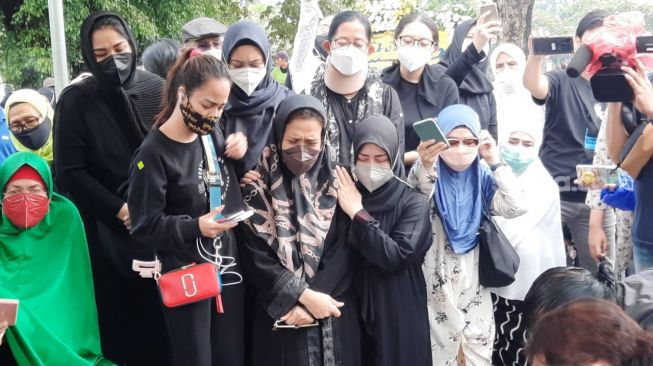 Chintami Atmanegara (depanm berhijab hitam dan masker putih) mencoba menguatkan istri Oddie Agam, Almafilia di pemakaman Oddie Agam di pemakaman Oddie Agam di TPU Menteng Pulo, Jakarta, Rabu (27/10/2021). [Evi Ariska/Suara.com]