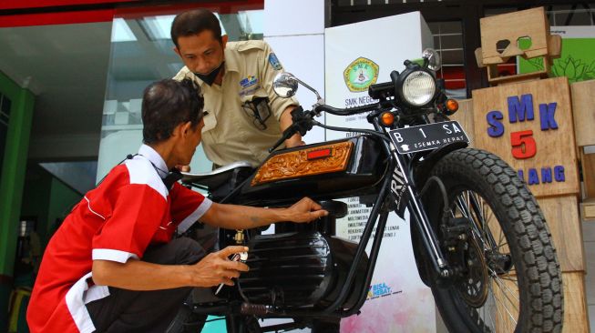 Kepala Sekolah Cone Kustarto (kanan) menunjukkan cara kerja purwarupa sepeda motor listrik hasil inovasinya di SMKN 5 Malang, Jawa Timur, Jumat (29/10/2021). ANTARA FOTO/Ari Bowo Sucipto
