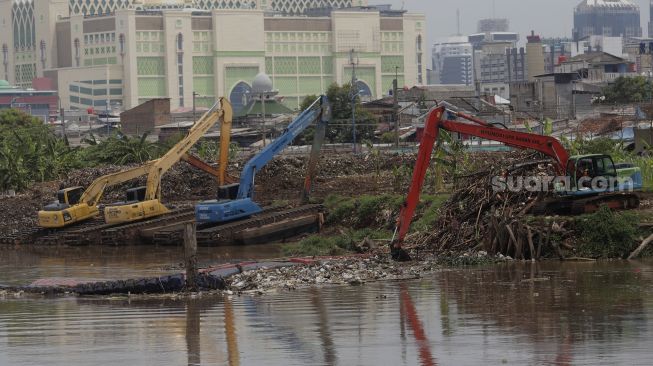 Petugas dari Suku Dinas Sumber Daya Air Jakarta Pusat mengoperasikan alat berat untuk mengangkut sampah di sepanjang aliran Kanal Banjir Barat di kawasan Tanah Abang, Jakarta, Jumat (29/10/2021). [Suara.com/Angga Budhiyanto]