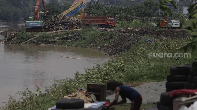 Petugas dari Suku Dinas Sumber Daya Air Jakarta Pusat mengoperasikan alat berat untuk mengangkut sampah di sepanjang aliran Kanal Banjir Barat di kawasan Tanah Abang, Jakarta, Jumat (29/10/2021). [Suara.com/Angga Budhiyanto]