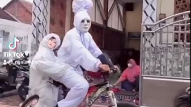 Kreatif! Pengamen Ini Cosplay Jadi Pocong Sambil Sepedaan dan Bonceng 'Anak'