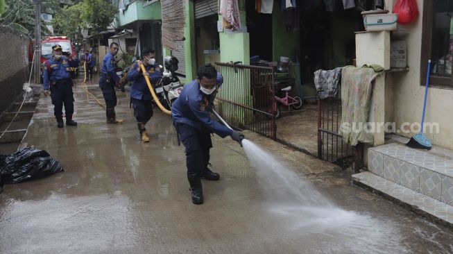 Petugas Penanggulangan Kebakaran dan Penyelamatan (Gulkarmat) membersihkan lumpur sisa banjir di Kelurahan Cipinang Melayu, Jakarta, Selasa (2/11/2021). [Suara.com/Angga Budhiyanto]