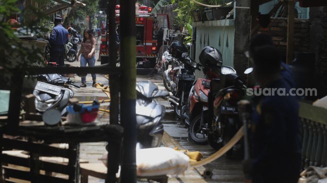 Warga berjalan di dekat mobil pemadam kebakaran saat proses pembersihan lumpur sisa banjir di Kelurahan Cipinang Melayu, Jakarta, Selasa (2/11/2021). [Suara.com/Angga Budhiyanto]