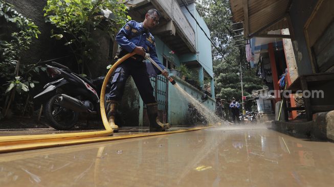 Petugas Penanggulangan Kebakaran dan Penyelamatan (Gulkarmat) membersihkan lumpur sisa banjir di Kelurahan Cipinang Melayu, Jakarta, Selasa (2/11/2021). [Suara.com/Angga Budhiyanto]