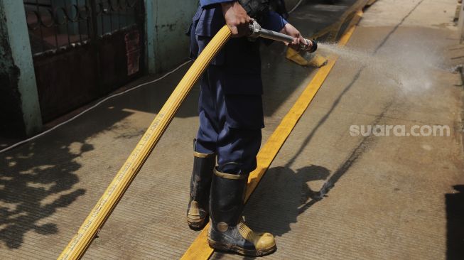 Petugas Penanggulangan Kebakaran dan Penyelamatan (Gulkarmat) membersihkan lumpur sisa banjir di Kelurahan Cipinang Melayu, Jakarta, Selasa (2/11/2021). [Suara.com/Angga Budhiyanto]