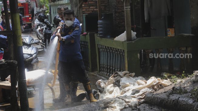 Petugas Penanggulangan Kebakaran dan Penyelamatan (Gulkarmat) membersihkan lumpur sisa banjir di Kelurahan Cipinang Melayu, Jakarta, Selasa (2/11/2021). [Suara.com/Angga Budhiyanto]