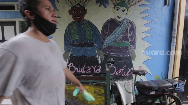 Warga berjalan melintasi mural bertema budaya Betawi di kawasan Kampung Sentra Kreatif, RW 006 Kota Bambu Selatan, Palmerah, Jakarta, Rabu (3/11/2021). [Suara.com/Angga Budhiyanto]