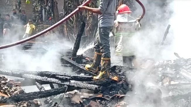 Petugas Damkar berusaha memadamkan api rumah warga yang terbakar. [Ist]