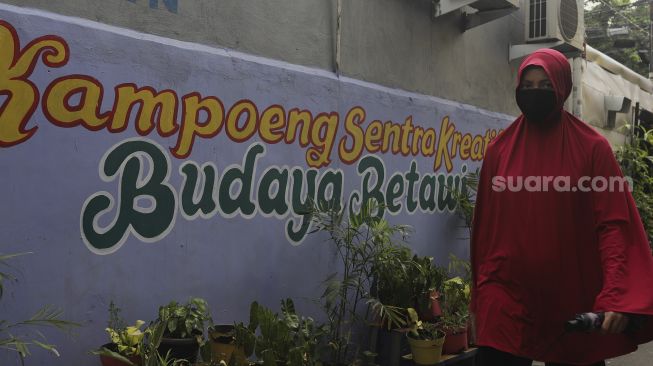 Warga berjalan melintasi mural bertema budaya Betawi di kawasan Kampung Sentra Kreatif, RW 006 Kota Bambu Selatan, Palmerah, Jakarta, Rabu (3/11/2021). [Suara.com/Angga Budhiyanto]