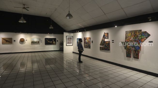 Pengunjung mengamati lukisan yang ditampilkan dalam pameran bertajuk "Hai, Kamu!", di Balai Budaya, Jakarta, Kamis (4/11/2021). [Suara.com/Angga Budhiyanto]