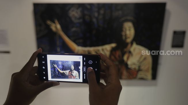 Pengunjung memotret lukisan yang ditampilkan dalam pameran bertajuk "Hai, Kamu!", di Balai Budaya, Jakarta, Kamis (4/11/2021). [Suara.com/Angga Budhiyanto]