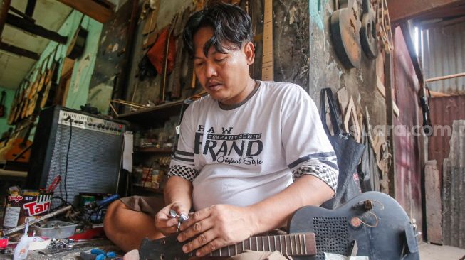 Pekerja menyelesaikan pembuatan gitar di sentra produksi dan reparasi gitar Pak Manto di Jalan Langgar II, Pejaten Timur, Pasar Minggu, Jakarta Selatan, Jumat (5/11/2021). [Suara.com/Alfian Winanto]