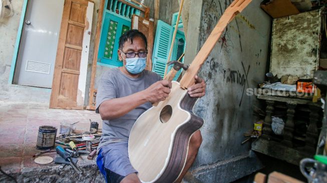 Pekerja menyelesaikan pembuatan gitar di sentra produksi dan reparasi gitar Pak Manto di Jalan Langgar II, Pejaten Timur, Pasar Minggu, Jakarta Selatan, Jumat (5/11/2021). [Suara.com/Alfian Winanto]