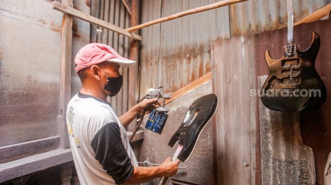 Pekerja mewarnai bagian gitar saat proses pembuatan di sentra produksi dan reparasi gitar Pak Manto di Jalan Langgar II, Pejaten Timur, Pasar Minggu, Jakarta Selatan, Jumat (5/11/2021). [Suara.com/Alfian Winanto]