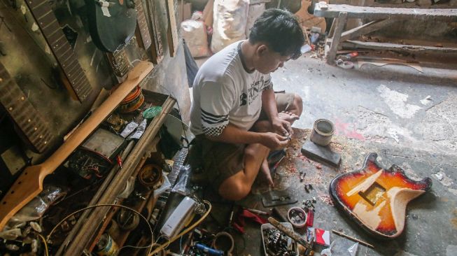 Pekerja menyelesaikan pembuatan gitar di sentra produksi dan reparasi gitar Pak Manto di Jalan Langgar II, Pejaten Timur, Pasar Minggu, Jakarta Selatan, Jumat (5/11/2021). [Suara.com/Alfian Winanto]