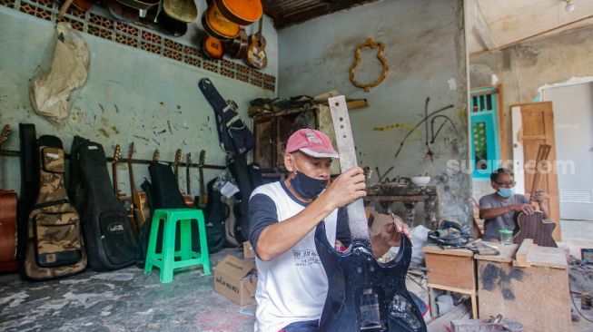 Pekerja menyelesaikan pembuatan gitar di sentra produksi dan reparasi gitar Pak Manto di Jalan Langgar II, Pejaten Timur, Pasar Minggu, Jakarta Selatan, Jumat (5/11/2021). [Suara.com/Alfian Winanto]