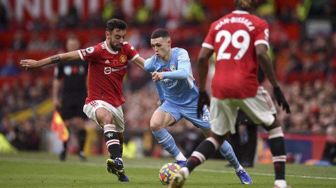 Gelandang Manchester City Phil Foden (tengah) bersaing dengan gelandang Manchester United Bruno Fernandes (kiri) dan bek Manchester United Aaron Wan-Bissaka selama pertandingan sepak bola Liga Utama Inggris antara Manchester United dan Manchester City di Old Trafford, Manchester, Inggris, Sabtu (6/11/2021). [OLI SCARFF / AFP]