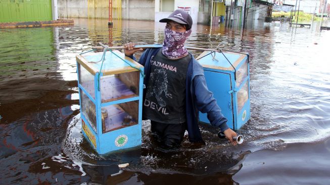 Seorang pedagang roti melintasi genangan banjir rob di Dumai, Riau, Sabtu (6/11/2021). ANTARA FOTO/Aswaddy Hamid
