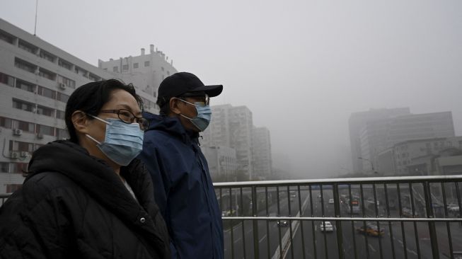 Orang-orang memakai masker berjalan di jalan layang pada hari yang berkabut dan tercemar di Beijing, China, Sabtu (6/11/2021). [JADE GAO / AFP]