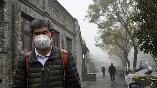 Seorang pria mengenakan masker berjalan di sepanjang jalan pada hari yang berkabut dan tercemar di Beijing, China, Sabtu (6/11/2021). [JADE GAO / AFP]