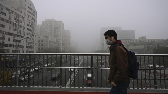 Warga memakai masker berjalan di jalan layang pada hari yang berkabut dan tercemar di Beijing, China, Sabtu (6/11/2021). [JADE GAO / AFP]