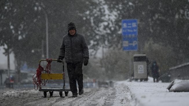 Seorang warga berjalan di jalan saat salju turun di Beijing, China, Minggu (7/11/2021). [NOEL CELIS / AFP]