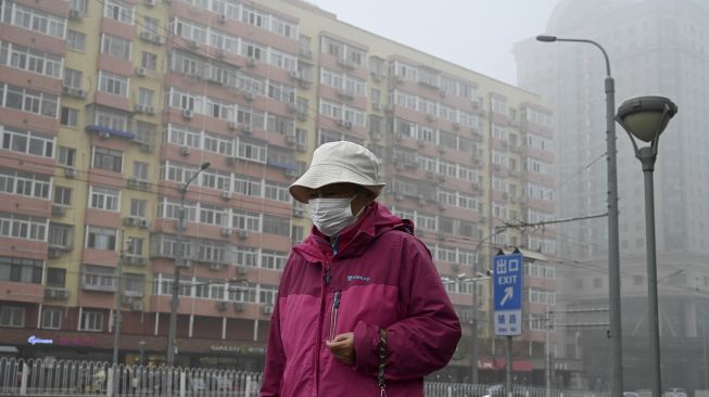 Warga mengenakan masker berjalan di sepanjang jalan pada hari yang berkabut dan tercemar di Beijing, China, Sabtu (6/11/2021). [JADE GAO / AFP]