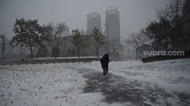 Seorang warga menggunakan kantong plastik sebagai penutup saat salju turun di Beijing, China, Minggu (7/11/2021). [NOEL CELIS / AFP]