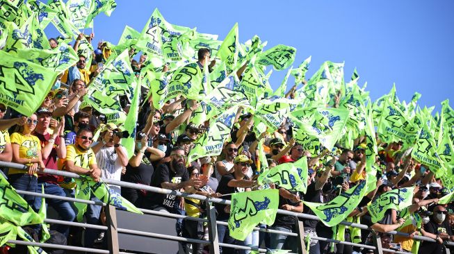 Fans pebalap Italia Valentino Rossi bersorak dari tribun selama balapan MotoGP Grand Prix Valencia di arena pacuan kuda Ricardo Tormo di Cheste, pada 14 November 2021. 
JOSE JORDAN / AFP