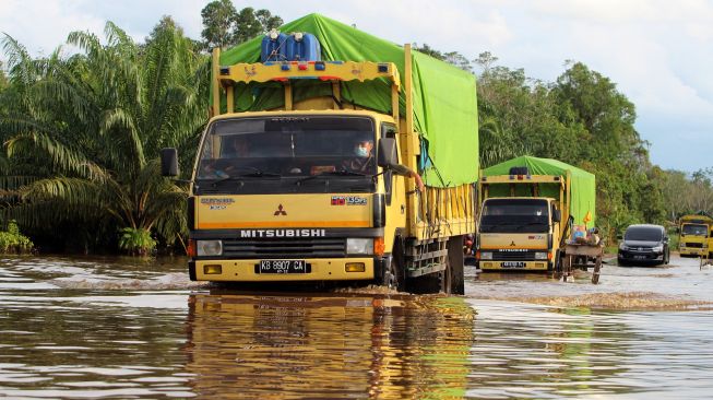 Beberapa truk dan mobil melintasi banjir yang merendam jalan nasional di Desa Peniti, Kabupaten Sekadau, Kalimantan Barat, Senin (15/11/2021). ANTARA FOTO/Jessica Helena Wuysang