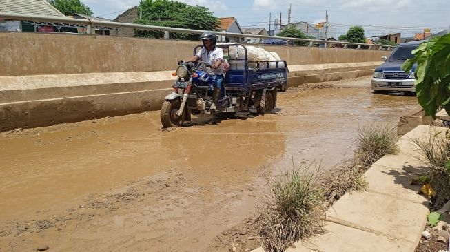 Pengendara melintasi area Jalan Bosih Raya Cibitung yang rusak parah, Selasa (16/11/2021).[Imam Fhaisal]