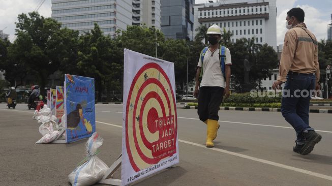 Pejalan kaki berjalan di dekat deretan mural Hari Kesehatan Nasional di kawasan Patung Arjuna Wiwaha, Jakarta, Rabu (17/11/2021). [Suara.com/Angga Budiyanto]