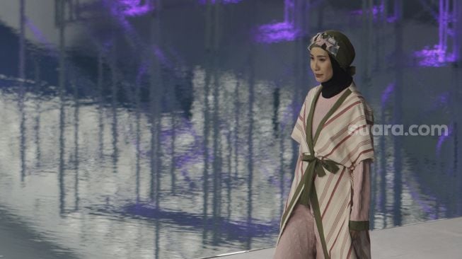 Model memperagakan busana muslim pada gelaran Jakarta Muslim Fashion Week (JMFW) di Stadion Aquatic, Gelora Bung Karno, Jakarta, Kamis (18/11/2021). [Suara.com/Angga Budhiyanto]