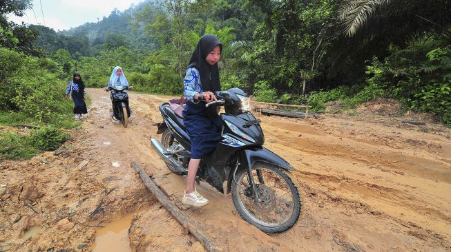 Pelajar melintasi jalan rusak menuju sekolah mereka di Desa Meribung, Limun, Sarolangun, Jambi, Kamis (18/11/2021). [ANTARA FOTO/Wahdi Septiawan]