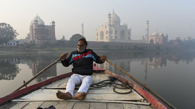 Seorang pria mengemudikan perahunya di Sungai Yamuna dekat Taj Mahal saat kondisi kabut asap di Agra, India, pada (16/11/2021). [SAJJAD HUSSAIN / AFP]