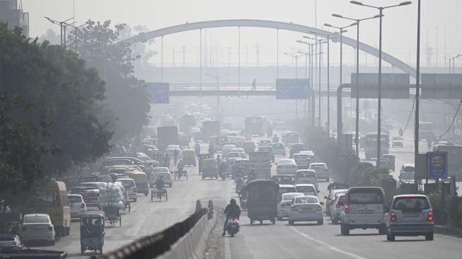Komuter berjalan di sepanjang jalan di tengah kabut asap tebal di New Delhi, India, pada (16/11/2021). [MONEY SHARMA / AFP]