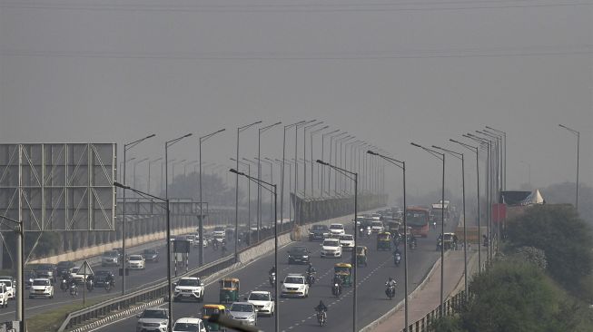 Komuter berjalan di sepanjang jalan di tengah kabut asap tebal di New Delhi, India, pada (16/11/2021). [MONEY SHARMA / AFP]